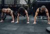 Three individuals performing push-ups together in a Mexico City gym setting.