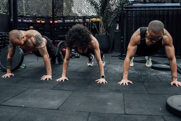 Three individuals performing push-ups together in a Mexico City gym setting.